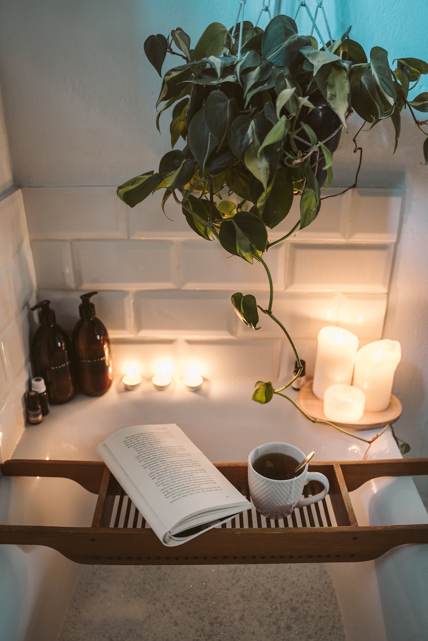 relaxing image, board across bath with book and a drink on it. in the background there are some lit candles.